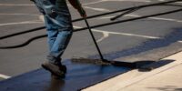 Worker,Using,A,Sealcoating,Brush,During,Asphalt,Resurfacing,Project