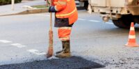 A road worker levels a fresh asphalt by a wooden level on a repaired road section in road construction