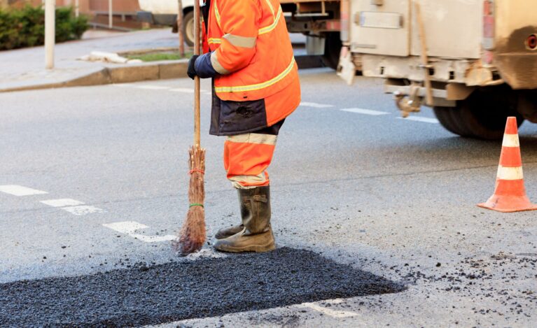 A road worker levels a fresh asphalt by a wooden level on a repaired road section in road construction
